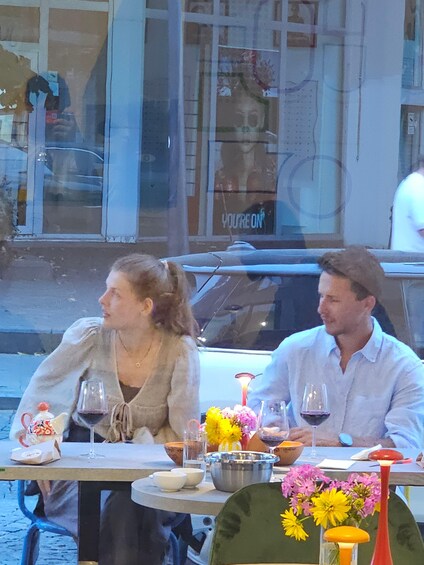 Two people seated at an outdoor table with wine glasses, a bowl, and flowers. 5