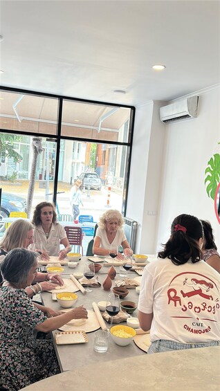 A group of people sitting around a table in a cafe, with a window view of a street outside. 2