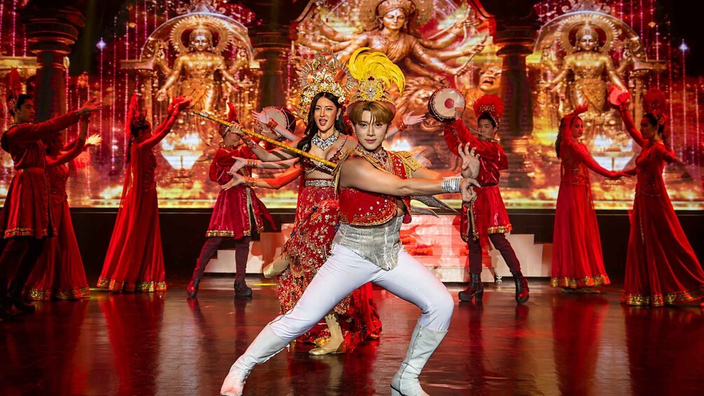 A stage with performers in traditional costumes, a large golden statue, and a backdrop with red lighting. 5