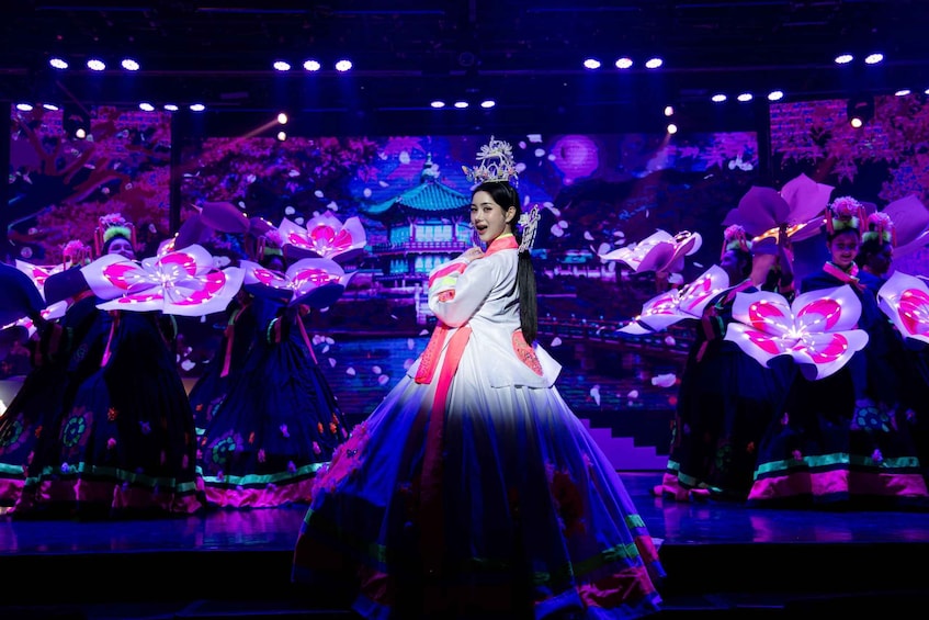A person in traditional attire with a tiara, surrounded by performers in similar costumes. 4
