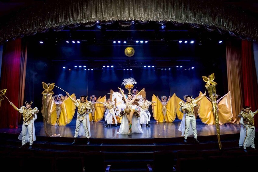 A stage with performers in golden and white costumes, a large golden emblem, and a backdrop of curtains. 3