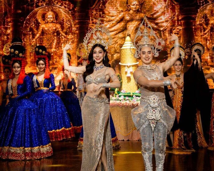 A group of dancers in elaborate costumes performing on a stage with a backdrop of a large statue. 1