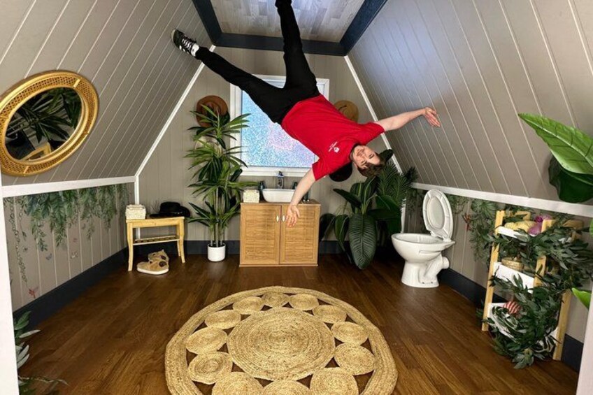 A person performing a handstand in a room with wooden flooring, a round woven rug, and various plants. 3