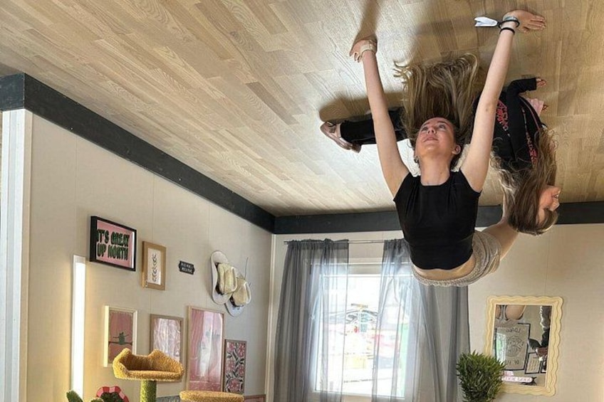 Two people performing an aerial dance routine in a room with wooden flooring, a window with curtains, and various wall decorations. 2
