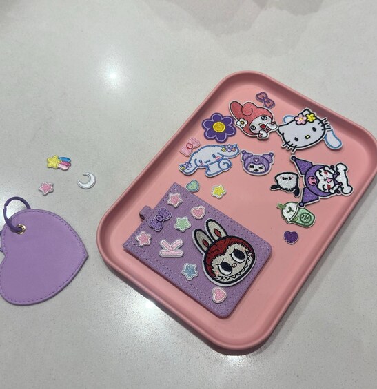 A pink tray with Hello Kitty and other cute character patches, a purple tag, and a crescent moon patch. 4