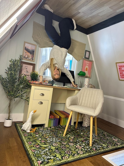 A person performing an acrobatic flip in a room with a desk, chair, potted plant, and various wall decorations. 5