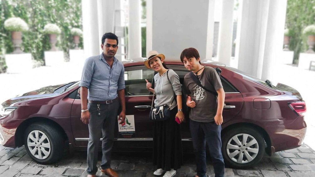 Three people standing in front of a maroon car with a sign that reads "LAKUPURNA TRAVELS". 5