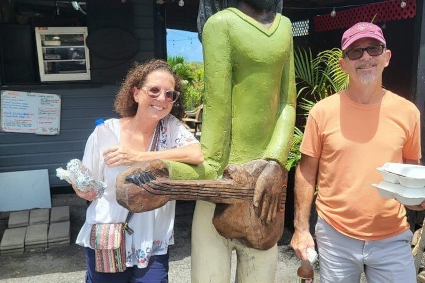 Two people standing next to a large wooden sculpture outdoors. 5