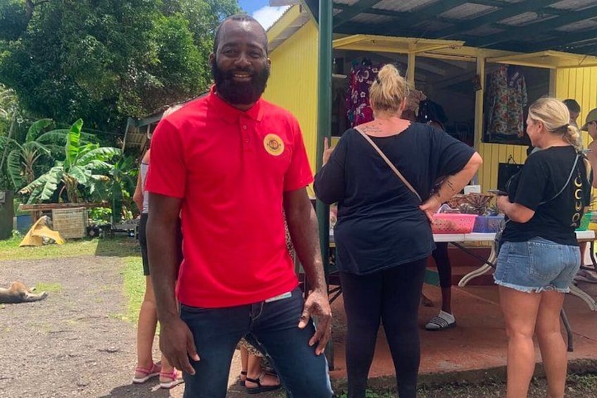 A man in a red shirt standing outdoors, with a building and people in the background. 1