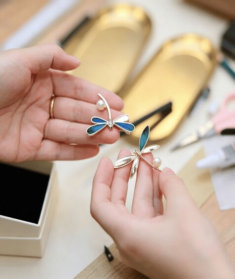 A person holding two butterfly-shaped earrings with a pearl. 4