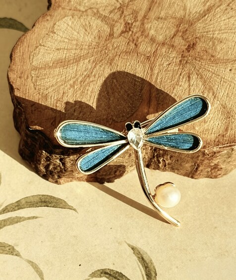 A dragonfly pin with a pearl on a wooden background. 5