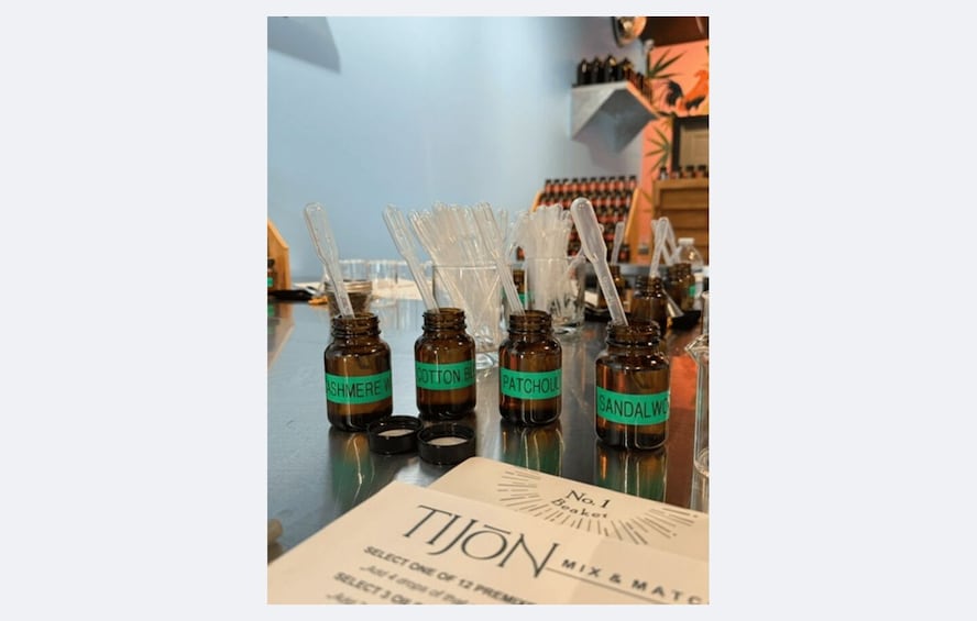 Bottles of essential oils with labels such as 'ASHMERE W,' 'COTTON BL,' 'PATCHOUL,' and 'SANDAL W' on a counter. 1