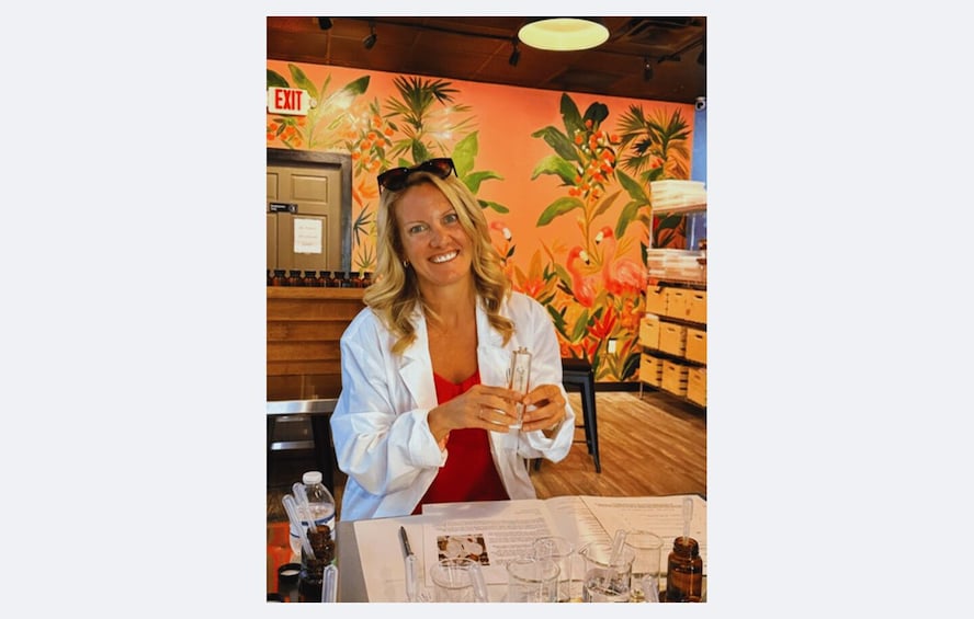 A person in a white lab coat holding a glass with a liquid, standing at a table with scientific equipment and papers, in a room with a tropical mural and an exit sign. 5