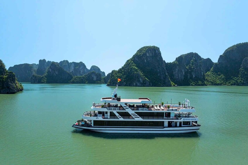 A large white boat with a flag on a calm river surrounded by green cliffs. 1