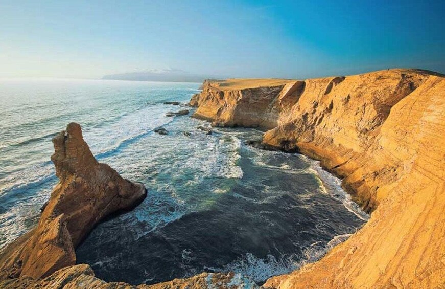 A coastal landscape with cliffs, a rocky outcrop, and the ocean. 5