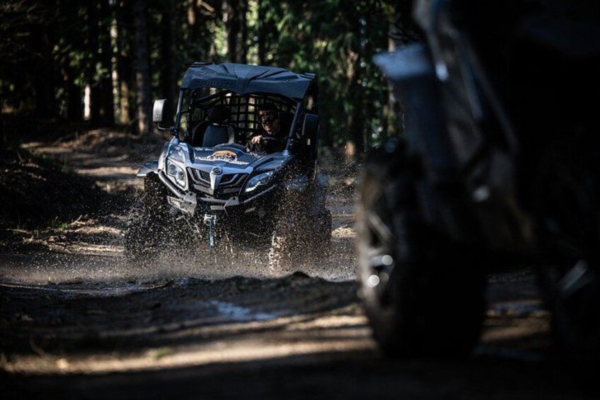 A vehicle driving through a forested area with water splashing around. 4