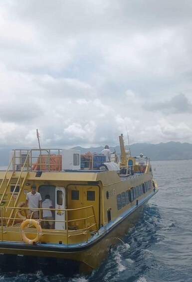 A yellow boat with people on board, moving through a body of water with mountains in the background. 2