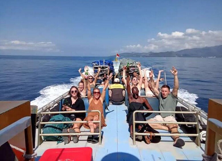 A group of people on a boat with raised hands, likely celebrating or cheering, with the ocean and distant mountains in the background. 3