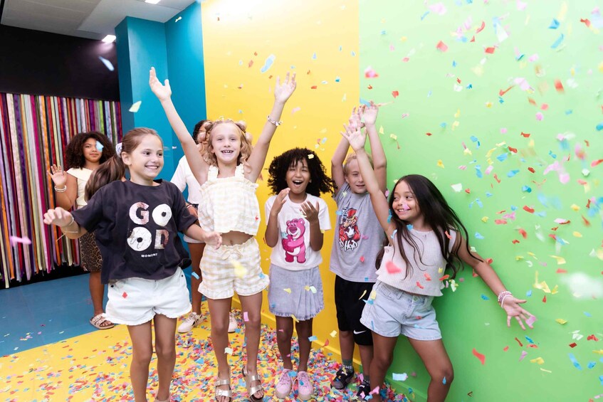Children playing with colorful paper confetti in a room with blue and yellow walls. 4