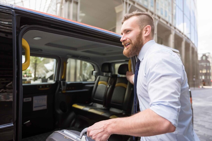 A man in a white shirt and tie stepping out of a black taxi with yellow interior accents. 1