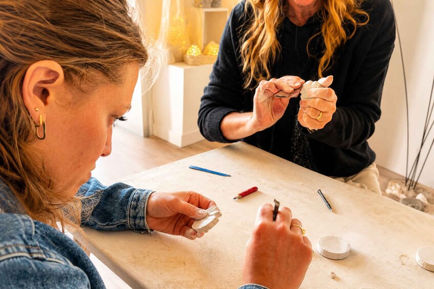Two people engaged in a craft activity, possibly pottery or sculpting, with tools and materials on a table. 1