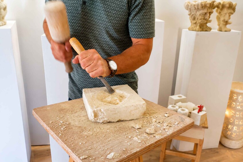 A person carving a block of wood on a workbench. 5