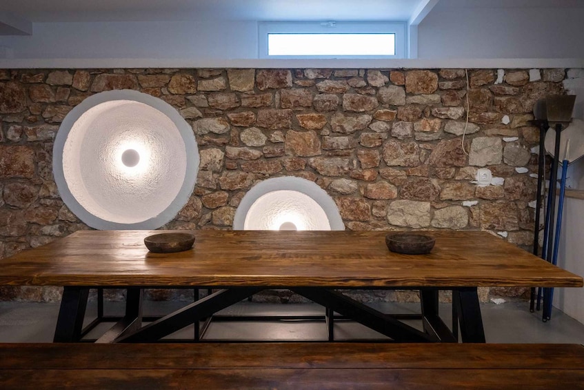 A wooden table with two bowls, a stone wall with circular light fixtures, and a skylight. 2