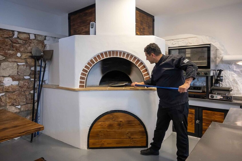 A person cleaning a brick oven in a kitchen with a stone wall and a wooden table. 4