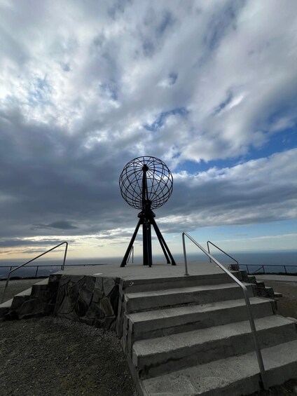 A satellite dish on a tripod with stairs leading up to it, overlooking a coastal area. 5