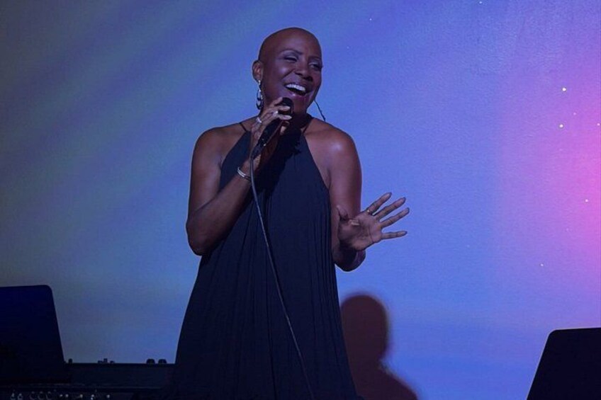A person speaking into a microphone on a stage with a blue and purple background. 2