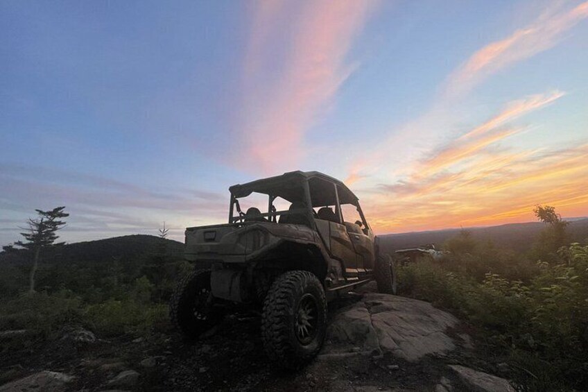 A 4x4 vehicle parked on a rocky outcrop with a sunset in the background. 3