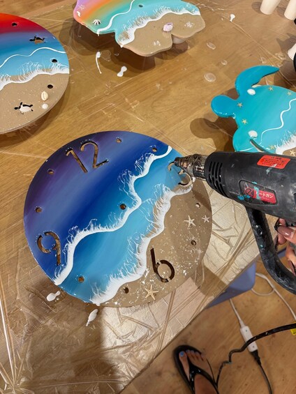 A person using a hot glue gun on a decorative object with a beach scene. 2