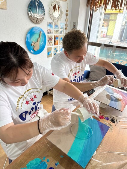 Two people painting on a canvas with various colors. 4