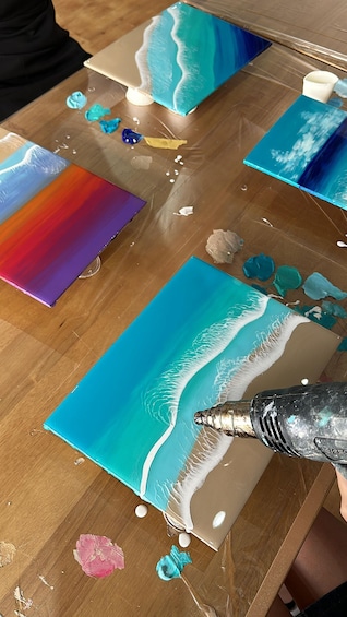 A painting in progress with a beach scene, featuring a blue ocean, white waves, and a sandy shore. 1