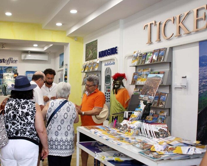 A bookstore with a 'TICKETS' sign, an 'AudioGuide' kiosk, and people browsing books. 2