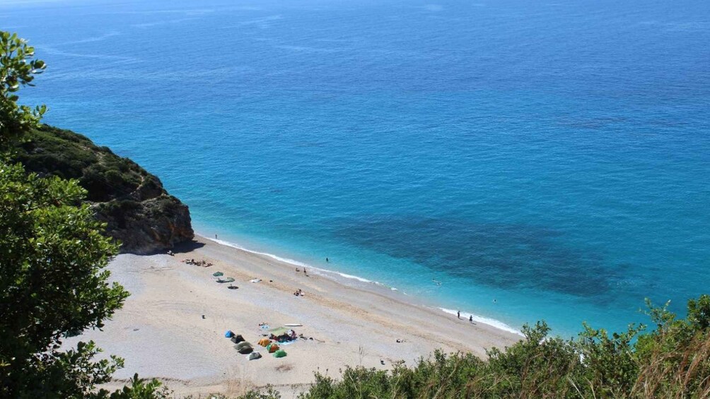 A beach with clear blue water, sandy shore, and some umbrellas. 4