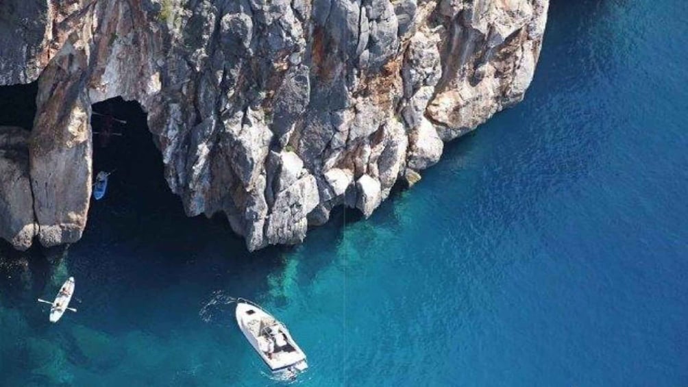 A rocky coastline with clear blue waters and two small boats anchored near the shore. 2