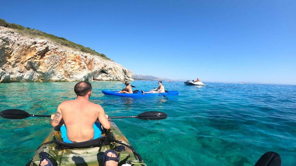 Two people kayaking on clear blue water with rocky cliffs in the background. 3