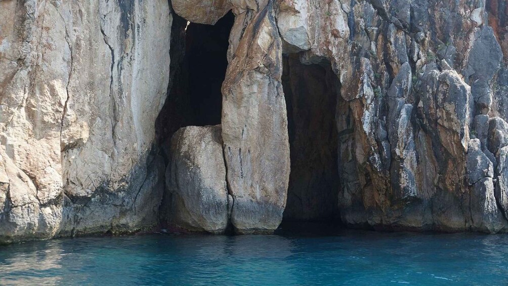 A natural rock formation with a cave entrance and clear blue water. 1