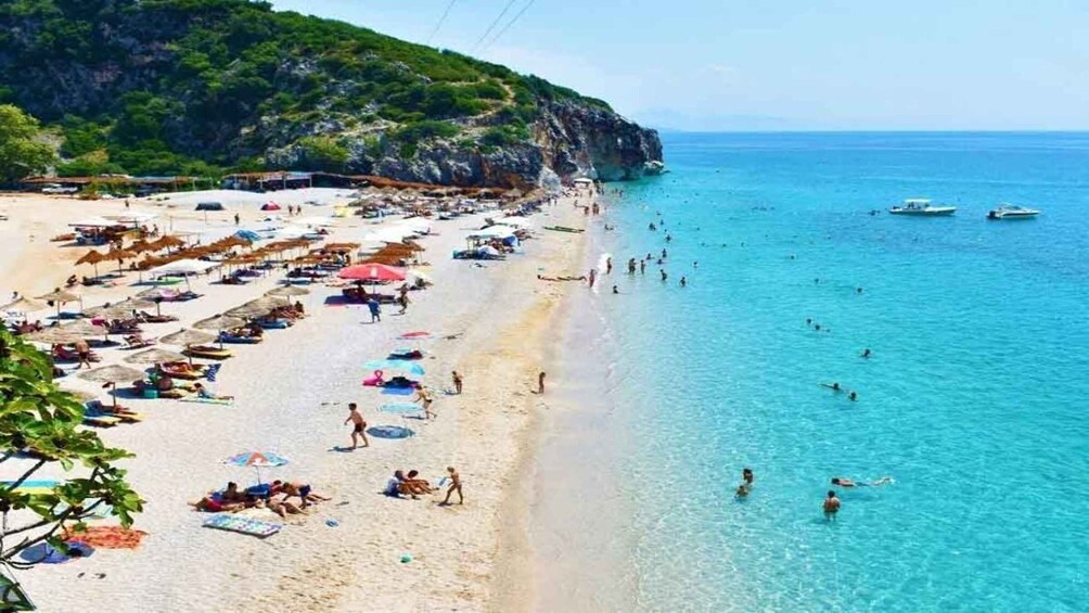 A beach with clear turquoise water, umbrellas, and people swimming. 5