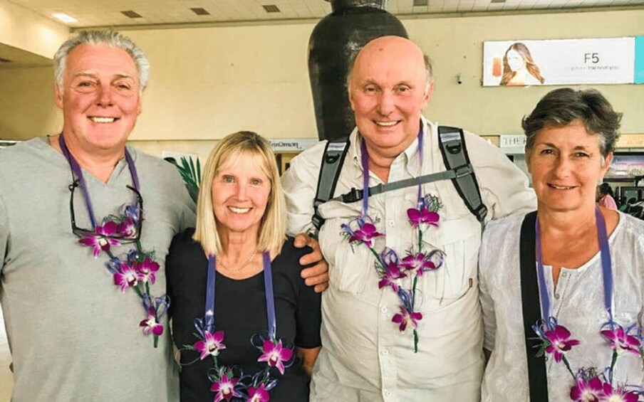 Four people standing indoors, wearing lanyards with purple flowers. 5