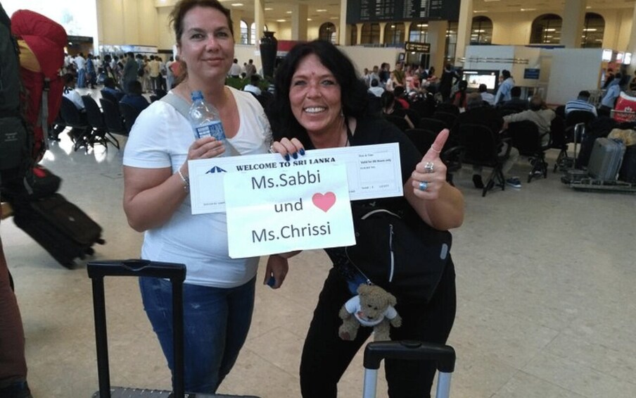 Two people holding a welcome sign for Ms. Sabbi and Ms. Chrissi at an airport. 3