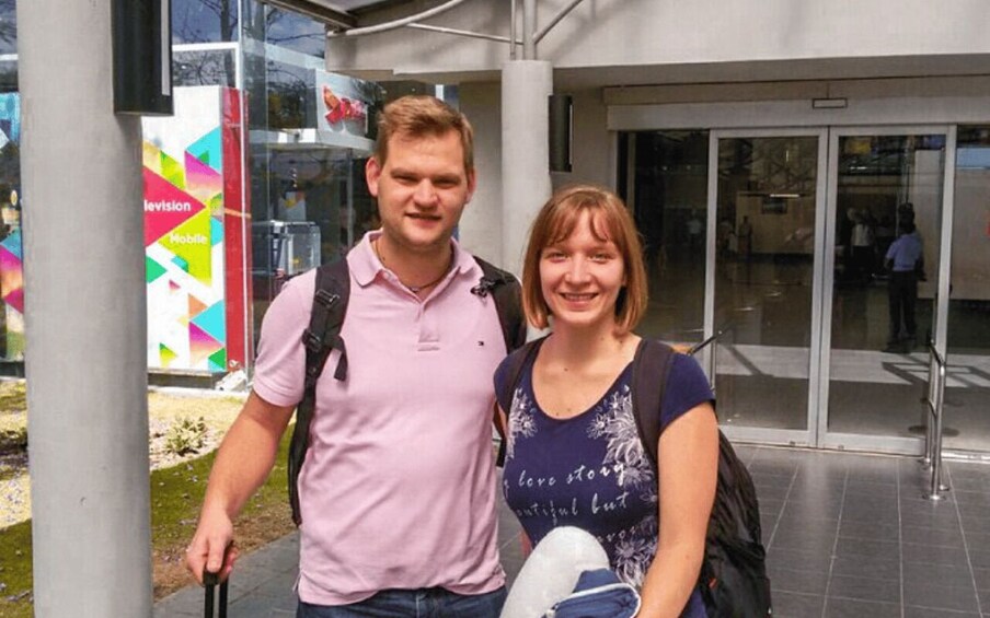 Two people standing in front of a building with a colorful sign. 1