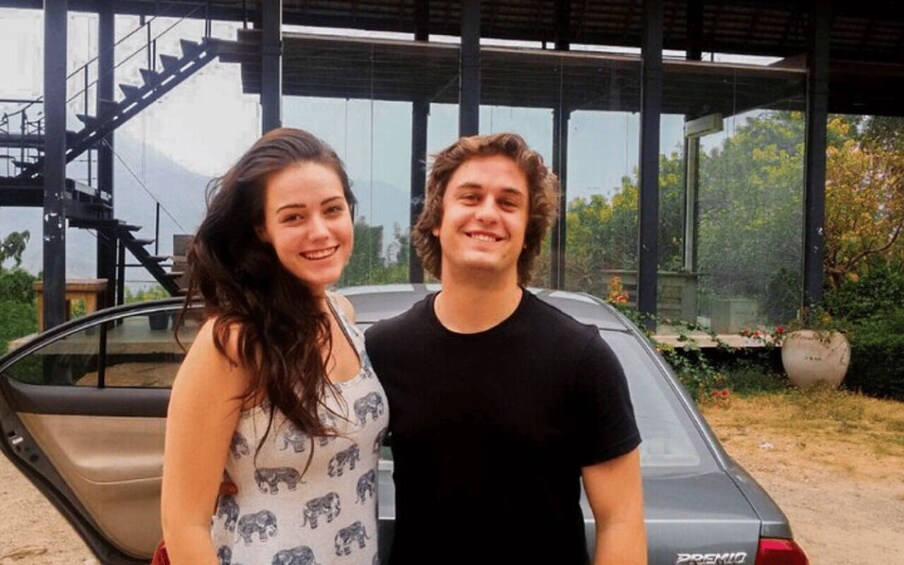 Two people standing in front of a car with a modern building and a staircase in the background. 4
