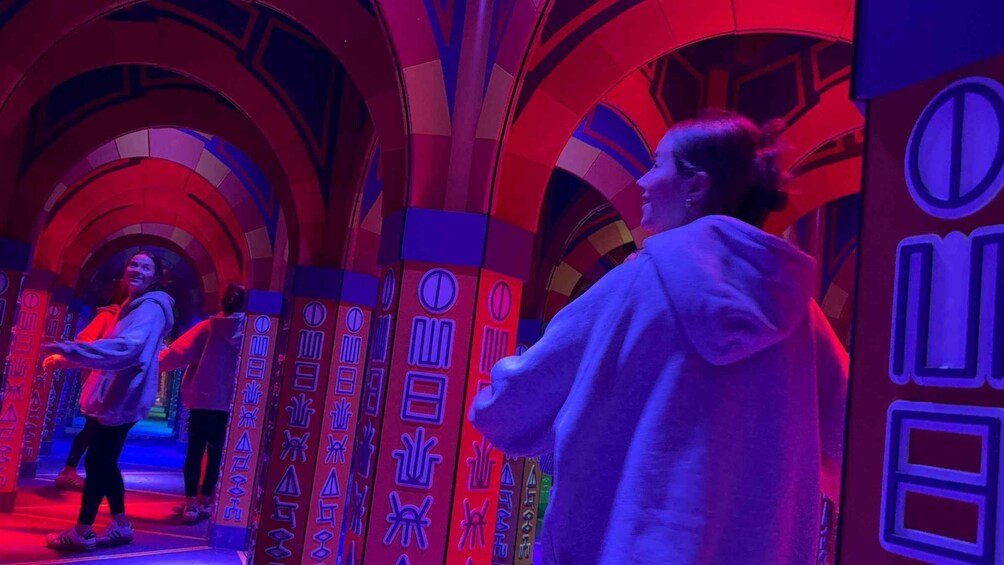 A person walking through a tunnel with arches and illuminated signs. 1