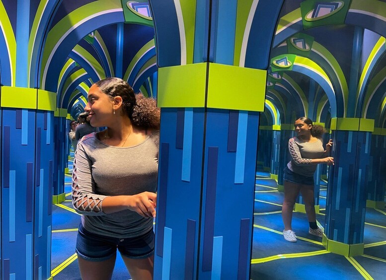 A person standing in a brightly colored, futuristic-themed hallway with blue and green tones and geometric patterns. 2