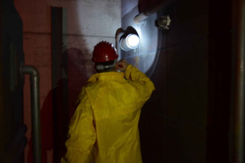 A person in a yellow safety jacket and red helmet working near a light fixture. 4