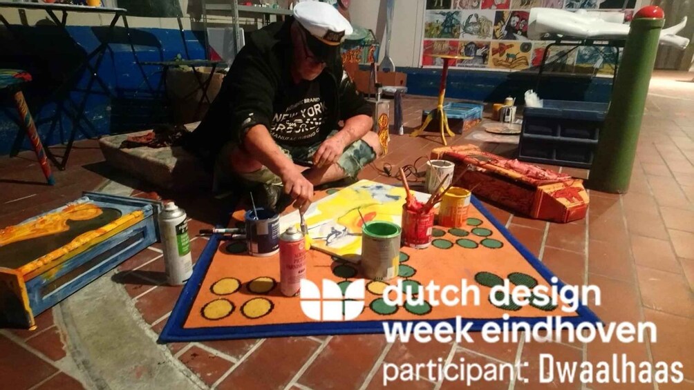 A person painting a colorful design on a mat with various paint cans and brushes. 3