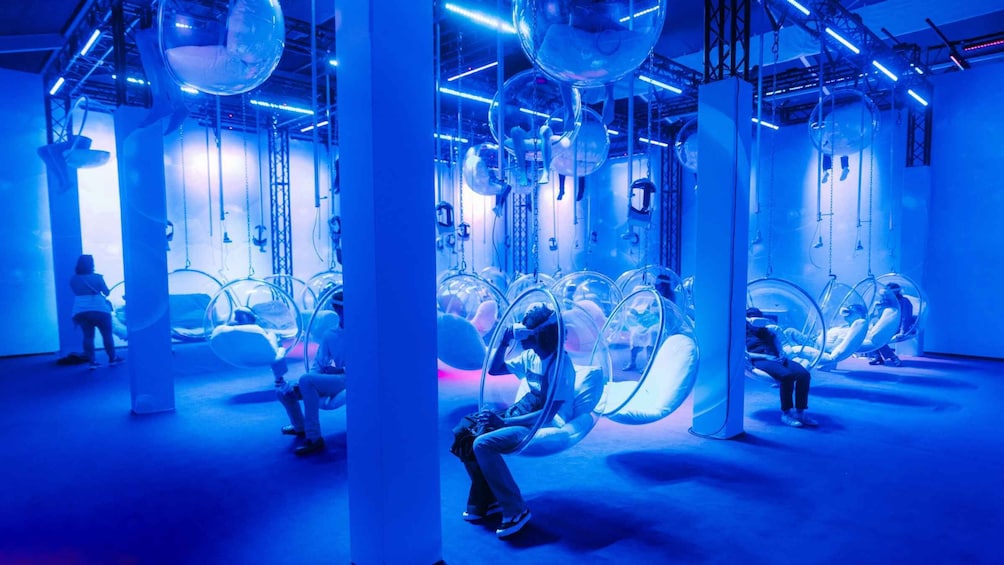 A room with people in transparent bubble chairs, blue lighting, and industrial elements. 5