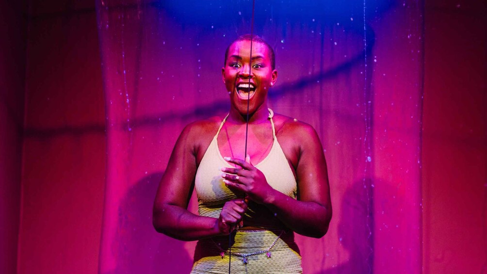 A person in a beige top and patterned skirt, standing in a room with a pink and blue gradient background. 4